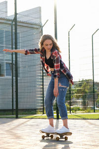 Full length portrait of smiling young woman standing on fence