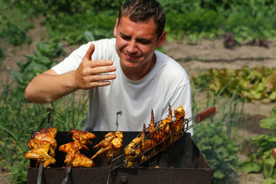 Young man cooking at a barbecue grill chicken wings. man smelling and enjoying picnic food. kindling