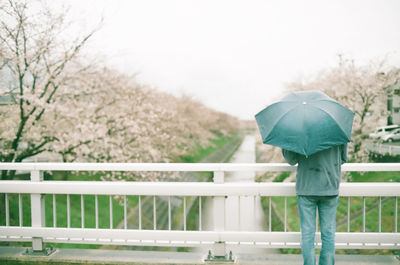 Man with umbrella standing on bridge over river against sky