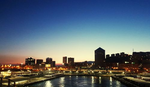 Illuminated buildings in city against clear blue sky