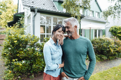 Smiling mature man looking at woman standing with hand on shoulder in backyard