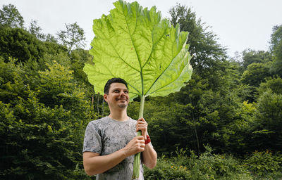 Portrait of young man photographing while standing on tree