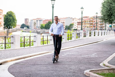 Young businessman in a suit riding an electric scooter while commuting to work in city