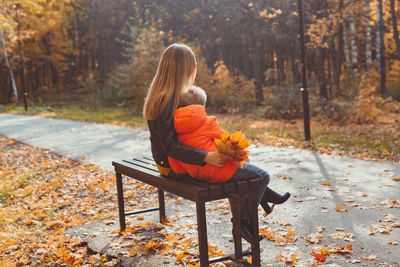 Rear view of woman sitting on sidewalk during autumn