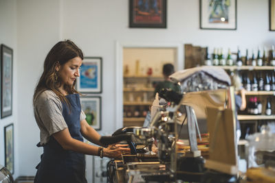 Side view of female sales clerk working at checkout counter in deli