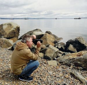 Man sitting on rock by sea against sky