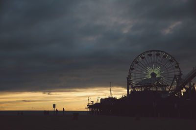 Silhouette santa monica pier and ferris wheel at beach against cloudy sky during sunset