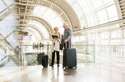 Full length of senior woman holding digital tablet by man standing with luggage at subway station