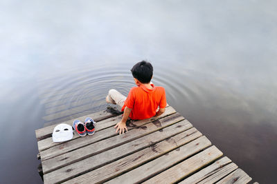 Rear view of boy sitting on pier over lake