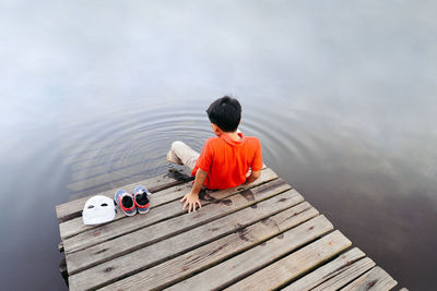 Rear view of boy sitting by lake on jetty