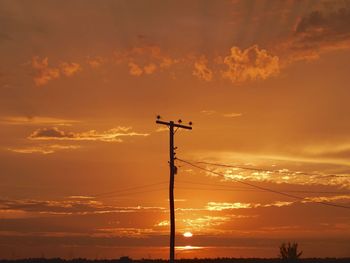 Low angle view of silhouette communications tower against dramatic sky during sunset