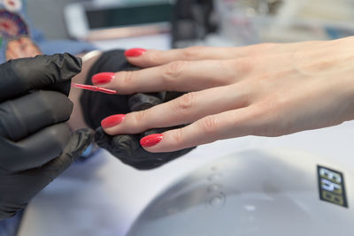 Cropped hands of manicurist applying nail polish on finger of woman