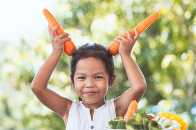 Portrait of girl holding carrots against tree