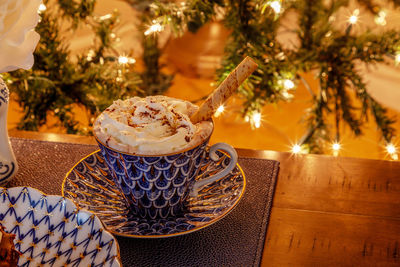 Cup of hot chocolate in a fancy bone china cup with gold and a silver spoon in front of a christmas