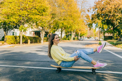 Girl sitting on longboard laughing on the road in autumn weather