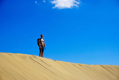 Shirtless man standing on sand against blue sky