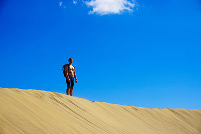 Shirtless man standing on sand against blue sky