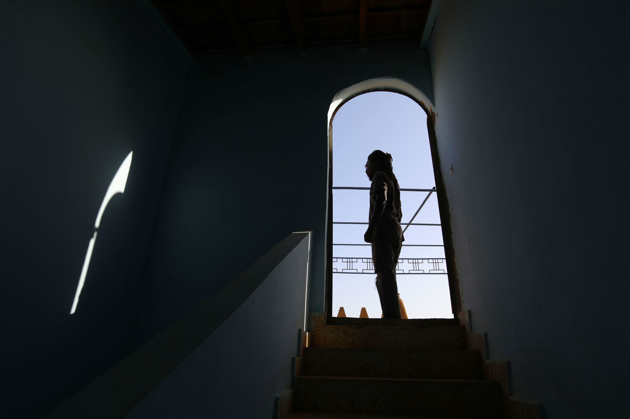 REAR VIEW OF WOMAN STANDING AGAINST STAIRCASE