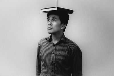 Man balancing book on head while standing by wall