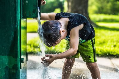 Boy washing hair from faucet at park during summer