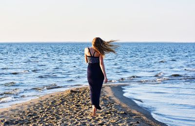 Rear view of woman walking at beach against clear sky