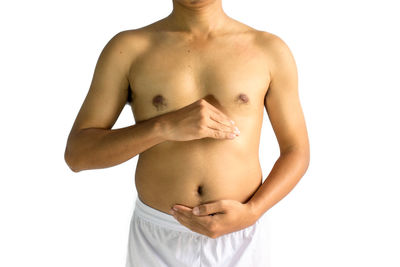 Midsection of shirtless young man touching belly while standing against white background