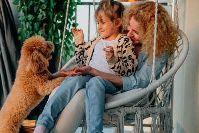 Happy mother and daughter with dog sitting at porch