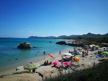 People at beach against clear blue sky