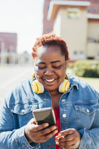 Happy woman with wireless headphones using smart phone in the street