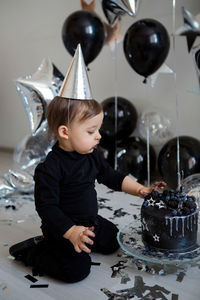 Boy stands next to a festive black cake and balloons