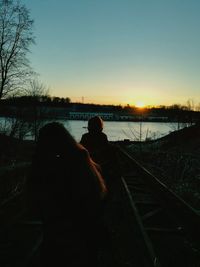 Silhouette of people sitting on shore against clear sky