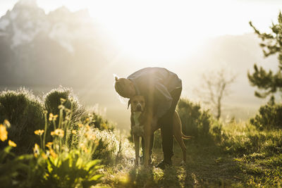 Man kissing dog while standing on field during sunny day