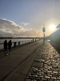 Rear view of people walking on footpath at sunset