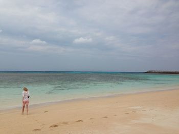 Rear view of woman standing on beach against sky