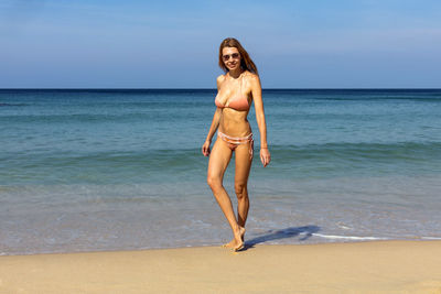 Young slim woman in bikini standing on sandy beach