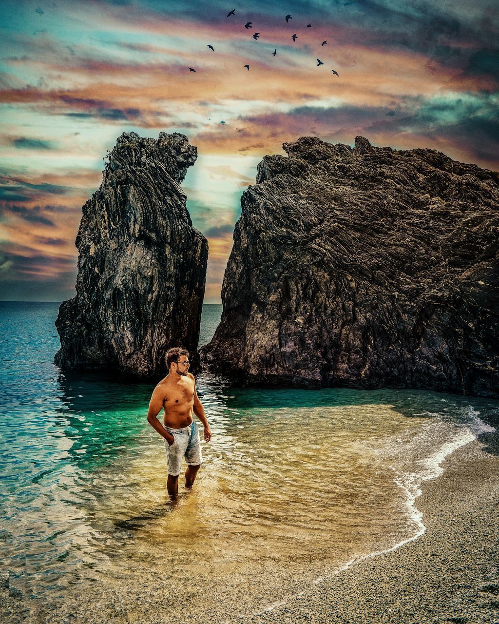 REAR VIEW OF MEN ON ROCK AT BEACH