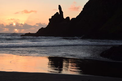 Silhouette rocks on beach against sky during sunset