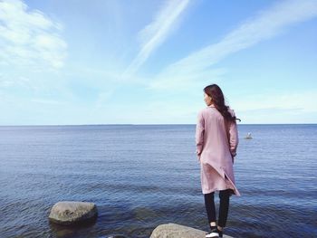 Rear view of woman looking at sea while standing on rock against sky