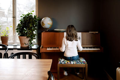 Rear view of girl playing piano while sitting in living room at home