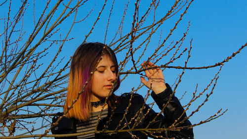 Low angle portrait of woman with bare tree against sky