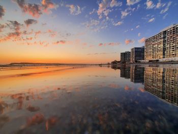 Scenic view of sea by buildings against sky during sunset