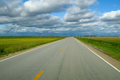 Empty road amidst field against sky