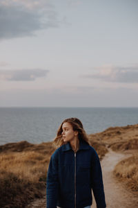 Young woman walking on dirt road against sea and sky
