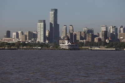 Sea by modern buildings against clear sky