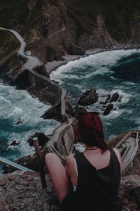 Rear view of woman sitting on cliff by sea