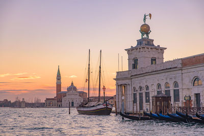 Boats in canal by buildings against sky during sunset