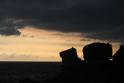 Silhouette rocks on shore against sky during sunset
