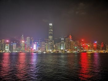 Illuminated city by sea against sky at night
