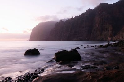 Rocks on beach against sky during sunset