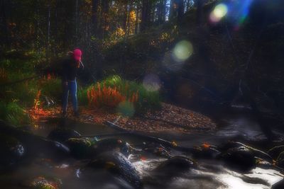 Blurred motion of man standing by waterfall in forest
